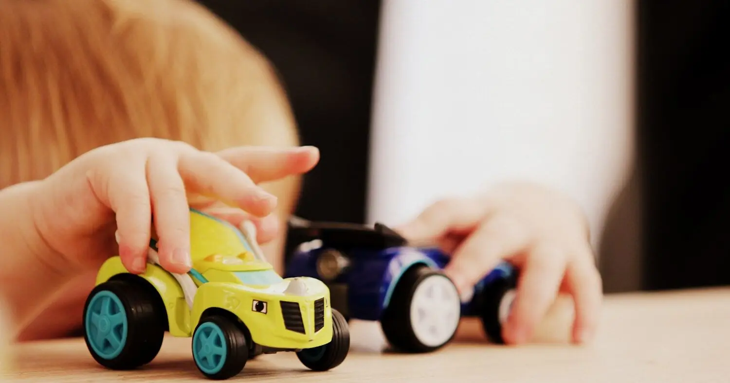Child playing with two toy cars on a wooden table